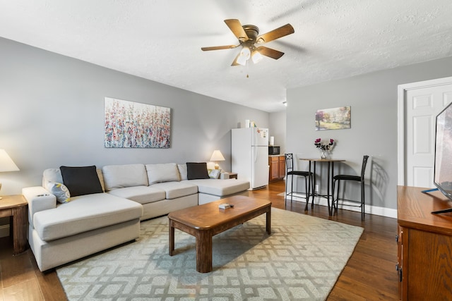 living room featuring dark wood-type flooring, ceiling fan, and a textured ceiling