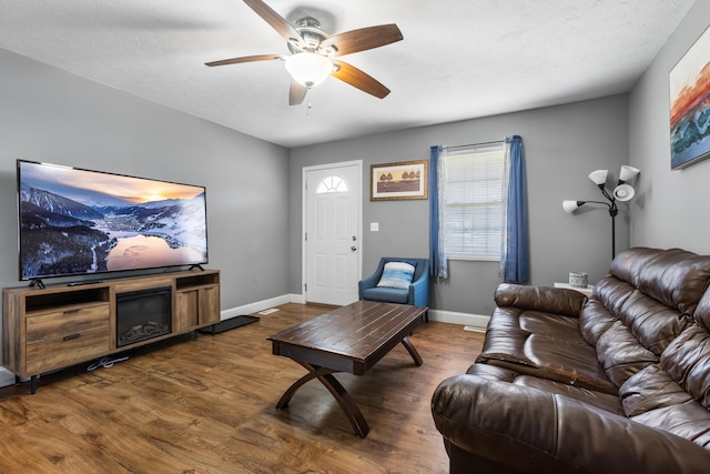 living room featuring dark wood-type flooring, ceiling fan, and a textured ceiling