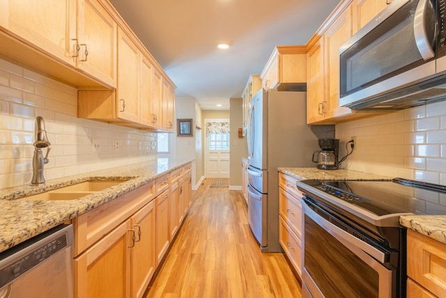 kitchen featuring sink, light stone counters, tasteful backsplash, appliances with stainless steel finishes, and light hardwood / wood-style floors