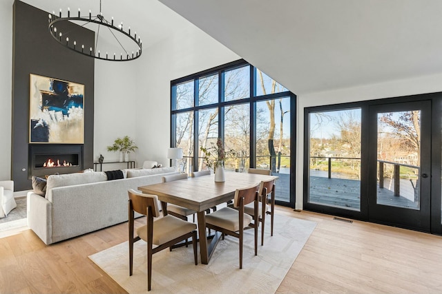 dining area with a large fireplace, visible vents, light wood-style flooring, and a high ceiling
