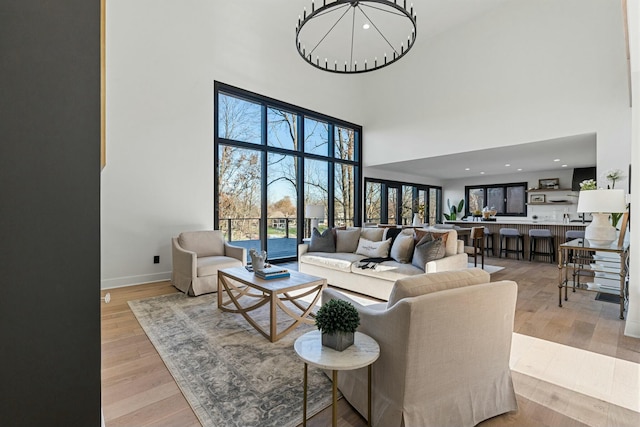 living area with light wood-type flooring, a towering ceiling, an inviting chandelier, and baseboards