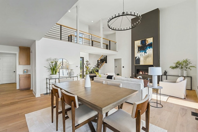 dining room with a high ceiling, an inviting chandelier, stairway, light wood-style flooring, and a lit fireplace