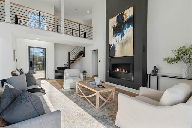 living area with stairway, a glass covered fireplace, recessed lighting, wood finished floors, and a high ceiling