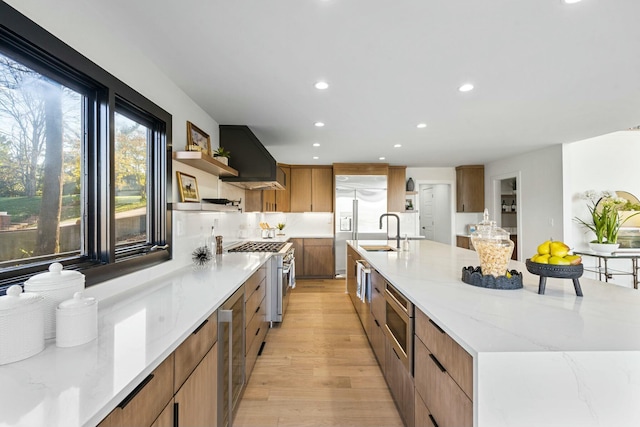 kitchen featuring a large island, sink, light hardwood / wood-style flooring, built in appliances, and custom exhaust hood