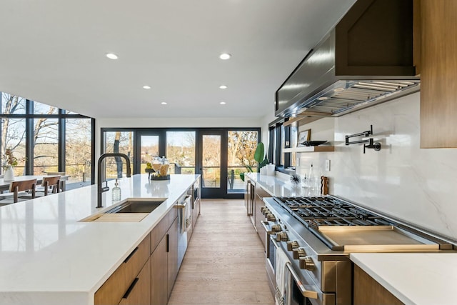 kitchen with sink, light wood-type flooring, appliances with stainless steel finishes, island exhaust hood, and a kitchen island with sink