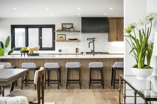 bar with backsplash, light hardwood / wood-style flooring, and wall chimney range hood