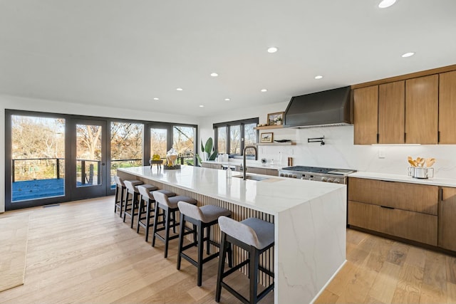 kitchen with a sink, a spacious island, premium range hood, light wood-type flooring, and recessed lighting