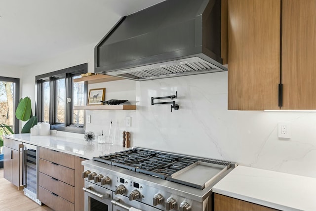 kitchen with beverage cooler, double oven range, brown cabinets, wall chimney exhaust hood, and modern cabinets