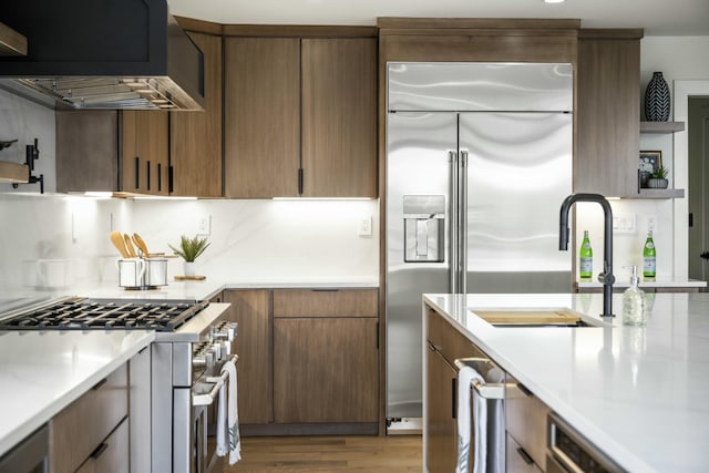 kitchen featuring wall chimney range hood, high quality appliances, light countertops, and a sink