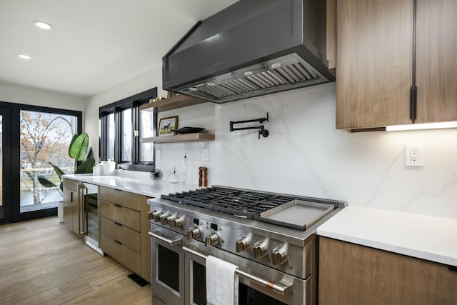 kitchen featuring double oven range, light wood-style floors, light countertops, ventilation hood, and wine cooler