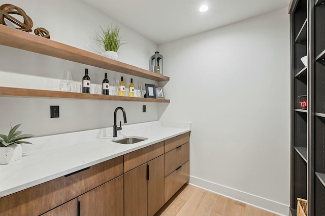 bar with light stone counters, sink, and light hardwood / wood-style flooring