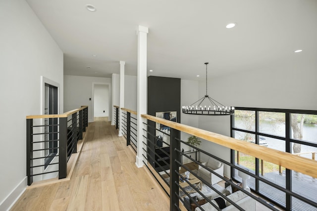 hallway with an upstairs landing, light wood-style flooring, a notable chandelier, and baseboards