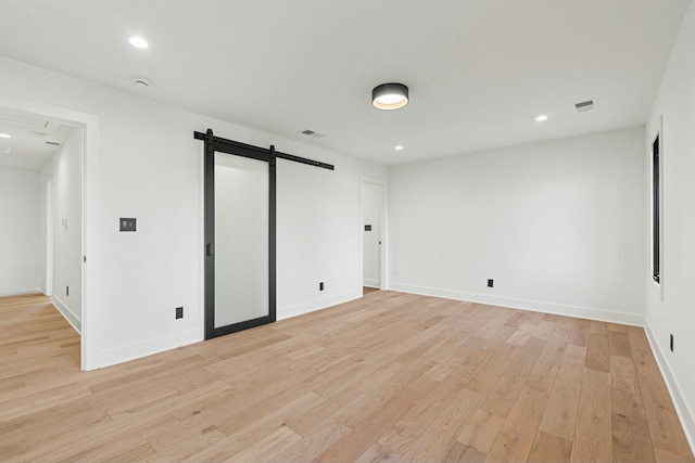 empty room with recessed lighting, a barn door, light wood-type flooring, visible vents, and baseboards