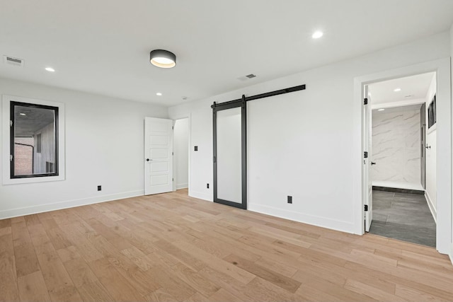 unfurnished bedroom featuring a barn door, baseboards, visible vents, and light wood-style floors