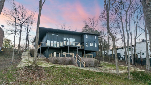 back of house at dusk featuring stairway and a wooden deck