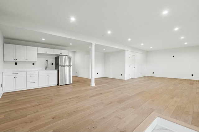 unfurnished living room with recessed lighting, light wood finished floors, baseboards, and a sink