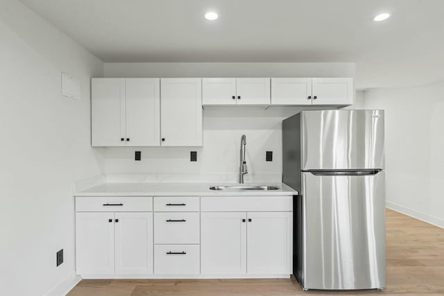 kitchen with white cabinets, a sink, freestanding refrigerator, baseboards, and recessed lighting