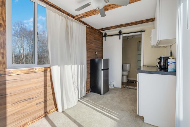 kitchen with stainless steel fridge, light colored carpet, a barn door, beamed ceiling, and wood walls