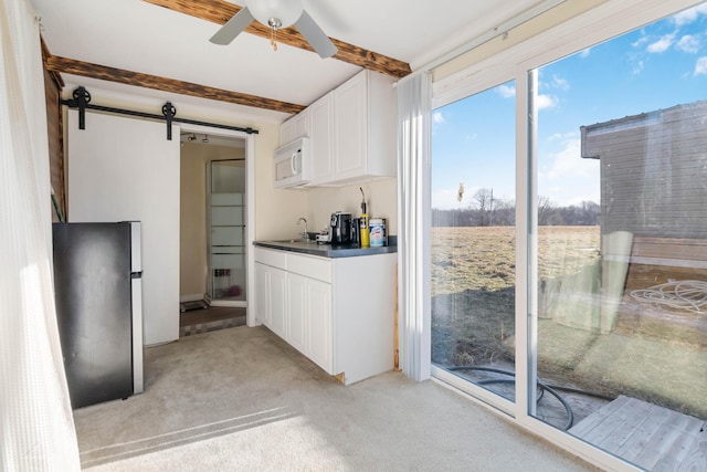 kitchen with stainless steel refrigerator, white cabinets, light colored carpet, a barn door, and beamed ceiling