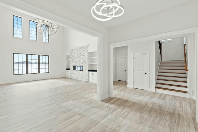 unfurnished living room featuring a chandelier, stairway, a glass covered fireplace, and light wood-style flooring