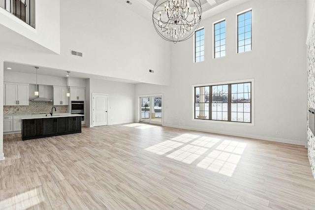 unfurnished living room with an inviting chandelier, a towering ceiling, and light wood-type flooring