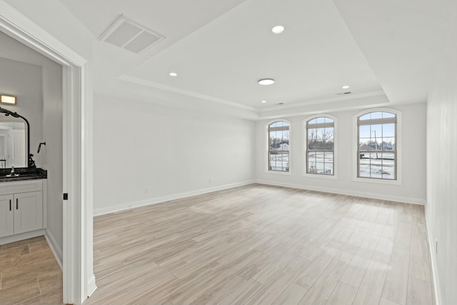 empty room featuring light wood-type flooring, a raised ceiling, visible vents, and a sink