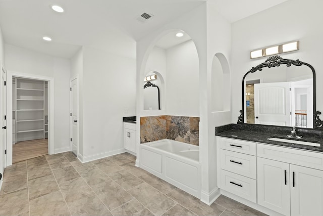 bathroom featuring a bath, two vanities, a sink, and a walk in closet