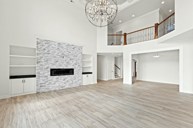 unfurnished living room with ornamental molding, built in shelves, a stone fireplace, and light wood finished floors