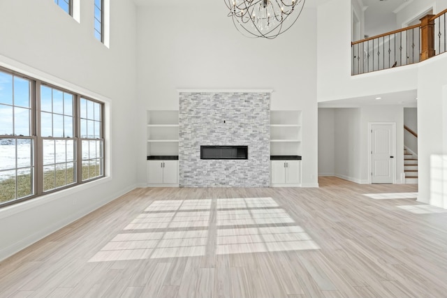 unfurnished living room with baseboards, a glass covered fireplace, light wood-style flooring, stairway, and a notable chandelier