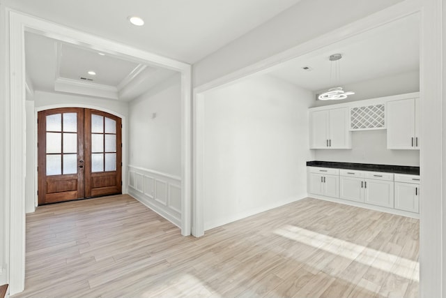 foyer entrance with a tray ceiling, french doors, arched walkways, light wood-style flooring, and wainscoting