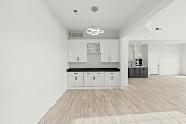 bar with hanging light fixtures, light wood finished floors, visible vents, and baseboards