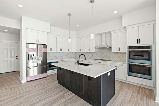 kitchen with stainless steel appliances, a sink, white cabinetry, wall chimney exhaust hood, and tasteful backsplash