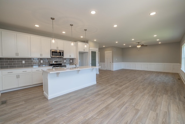 kitchen featuring pendant lighting, stainless steel appliances, light hardwood / wood-style floors, an island with sink, and white cabinets