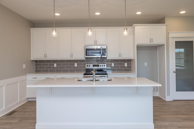 kitchen featuring sink, white cabinetry, decorative light fixtures, appliances with stainless steel finishes, and a kitchen island with sink