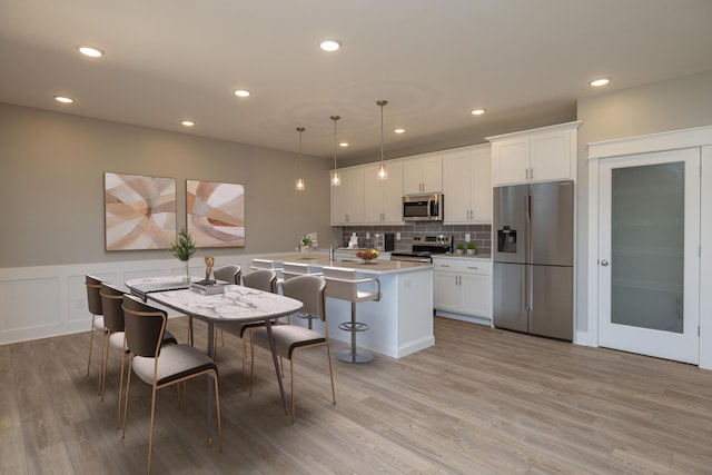 kitchen with appliances with stainless steel finishes, a kitchen breakfast bar, decorative backsplash, white cabinets, and decorative light fixtures