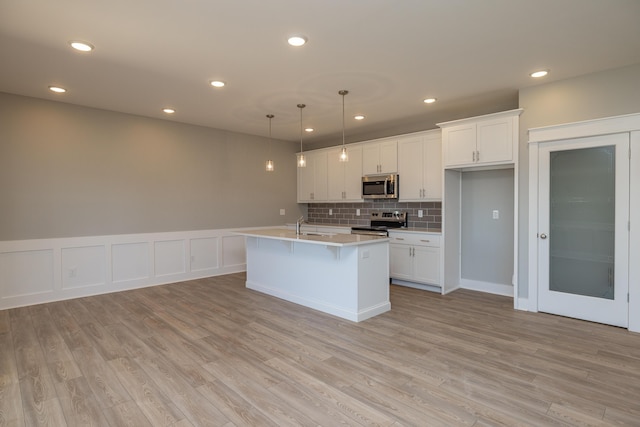 kitchen with white cabinetry, decorative light fixtures, stainless steel appliances, and a center island with sink