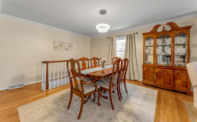 dining room with ornamental molding and light hardwood / wood-style flooring