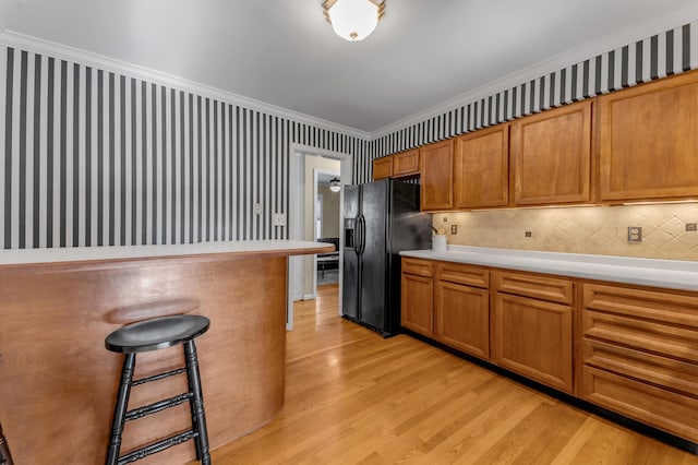 kitchen with light hardwood / wood-style flooring, a breakfast bar, backsplash, ornamental molding, and black refrigerator with ice dispenser