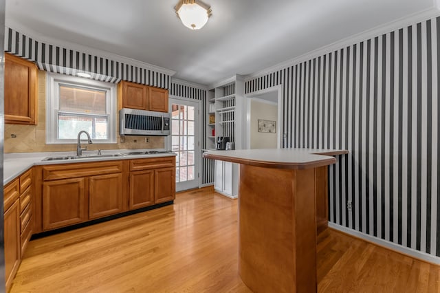 kitchen with sink, crown molding, tasteful backsplash, white gas stovetop, and light wood-type flooring