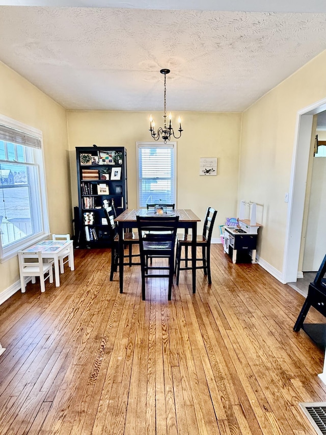 dining room with wood-type flooring, a wealth of natural light, a notable chandelier, and a textured ceiling