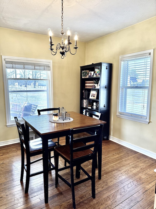 dining room with dark wood-type flooring, a healthy amount of sunlight, an inviting chandelier, and a textured ceiling