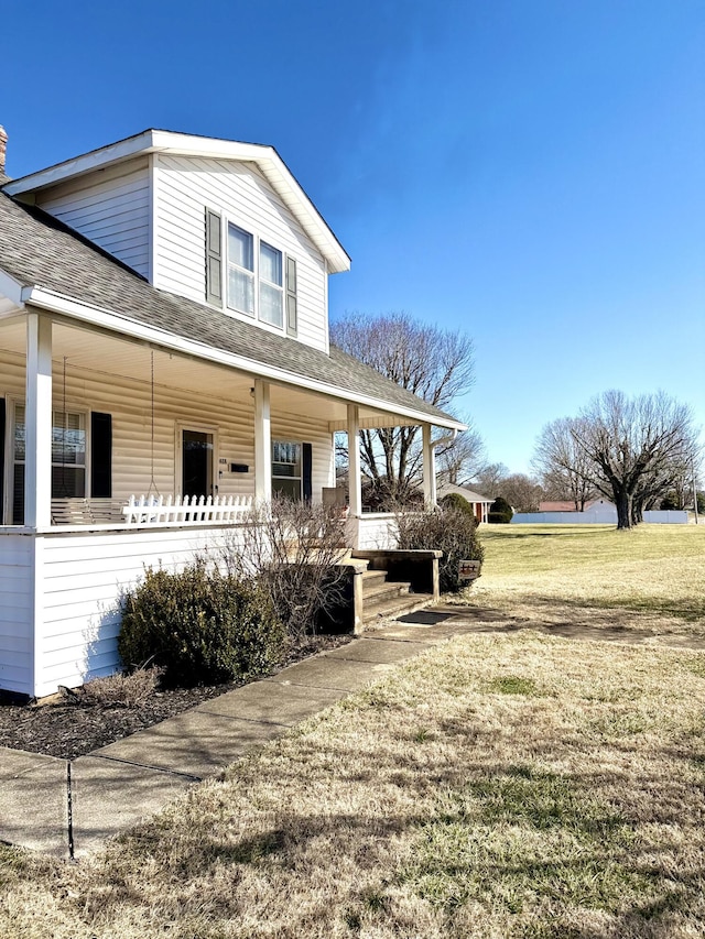 view of side of property featuring covered porch and a lawn