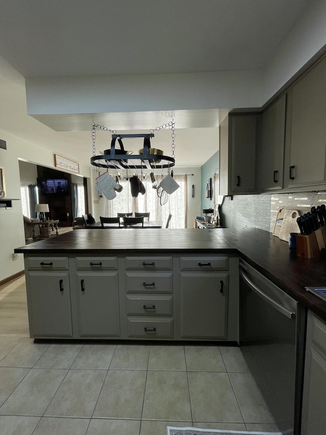 kitchen with light tile patterned floors, gray cabinetry, decorative backsplash, stainless steel dishwasher, and kitchen peninsula