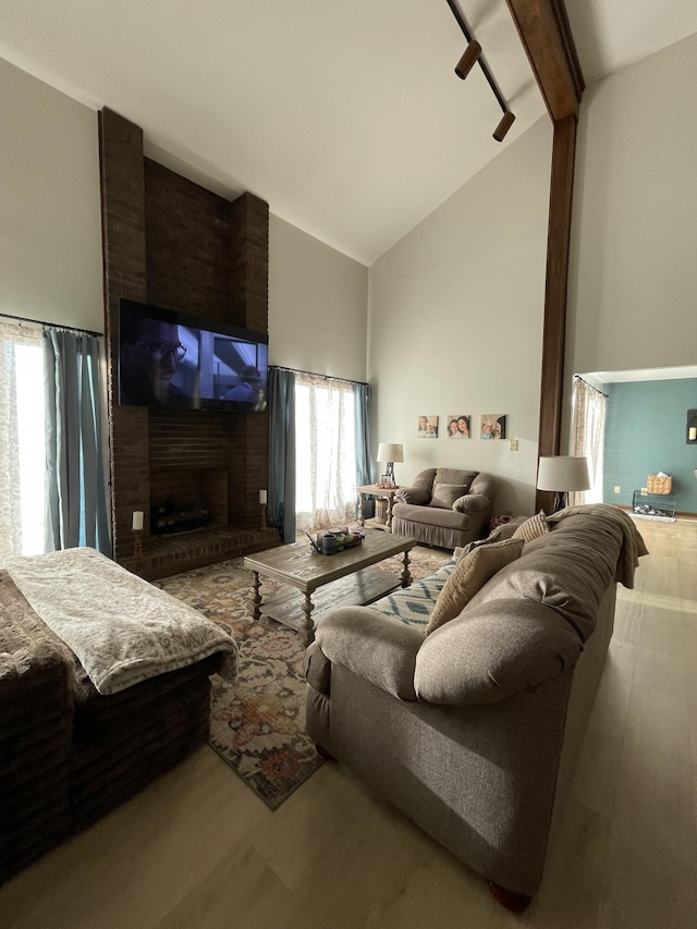 living room with beam ceiling, high vaulted ceiling, and a brick fireplace