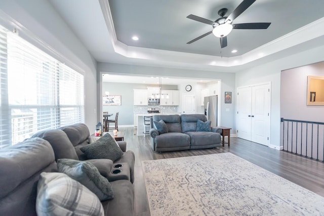 living area with dark wood-style flooring, recessed lighting, a raised ceiling, a ceiling fan, and baseboards