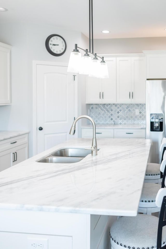 kitchen with stainless steel fridge with ice dispenser, light stone countertops, a kitchen bar, white cabinetry, and a sink