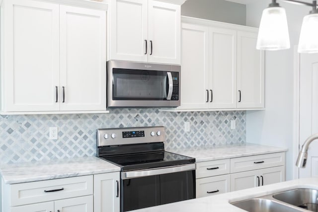 kitchen featuring white cabinets, a sink, hanging light fixtures, stainless steel appliances, and backsplash