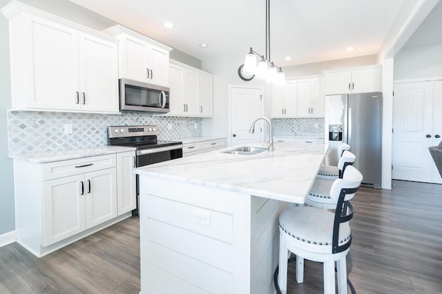 kitchen with dark wood-style flooring, a breakfast bar area, appliances with stainless steel finishes, white cabinetry, and a sink