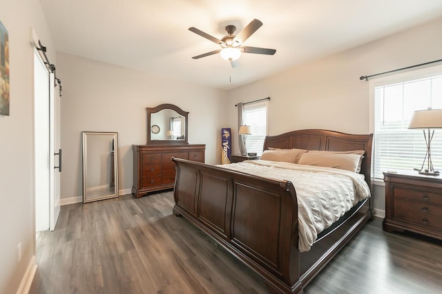 bedroom with ceiling fan, a barn door, dark wood finished floors, and baseboards