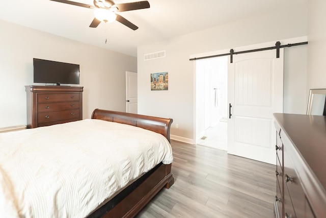 bedroom with a barn door, baseboards, visible vents, a ceiling fan, and light wood-style flooring